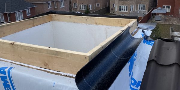 A rooftop view shows a dormer construction in progress, expertly handled by a roofing contractor. The structure is wrapped in white Soprema material with black roofing tiles partially installed. Suburban houses and a cloudy sky provide the backdrop for this skylight repair metal roofing project.