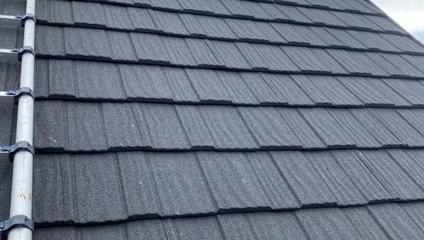A gray tiled roof under a cloudy sky hints at recent roof repair. A metal ladder, resting on the left side, suggests the work of a roofing contractor. The top section is securely covered with a blue tarp, awaiting completion.