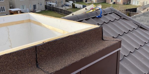 A rooftop view reveals a residential neighborhood with rows of houses. Scattered roofing materials, including an oxygen tank and a metal tool, hint at ongoing work by a roofing contractor. Power lines and cloudy skies frame the scene, where skylight replacement is likely underway.
