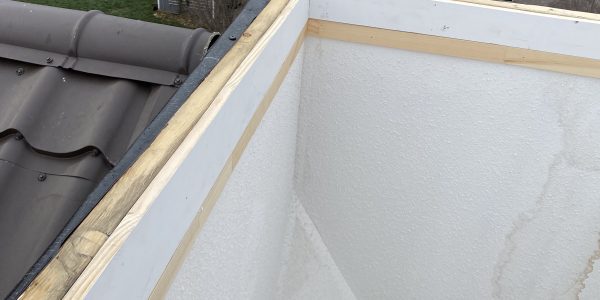 The view from the roof reveals a large, open chimney or shaft lined with white material and wooden framing, showcasing the impeccable work of a dedicated roofing company. In the background, residential houses and trees complete the picturesque scene.