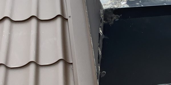 A close-up of a rooftop with gray, tile-like panels showcases expert skylight replacement. A large window structure with metal framing and visible sealant sits in the center. In the background, red and beige brick buildings complete the scene, highlighting professional craftsmanship in skylight repair.