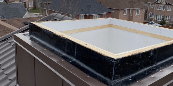 A rooftop with a central box-like structure, possibly needing roof repair, is surrounded by shingles. Suburban houses and a cloudy sky form the backdrop, hinting at a roofing contractors next project.