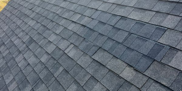 A close-up view of a gray shingle roof, expertly installed by a roofing contractor, showcases two vents. The sky is partly cloudy, and trees with autumn leaves add a picturesque backdrop.