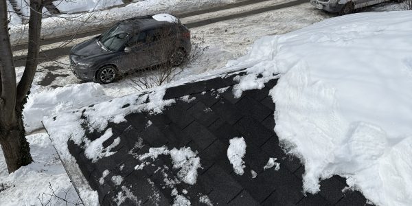 A snowy rooftop offers a serene view of a street lined with houses, reflecting the tranquility of winter. Two cars rest on the snow-draped road, while leafless trees stand guard. Its a scene that might tempt any roofing contractor to dream of skylight repair opportunities beneath such picturesque eaves.